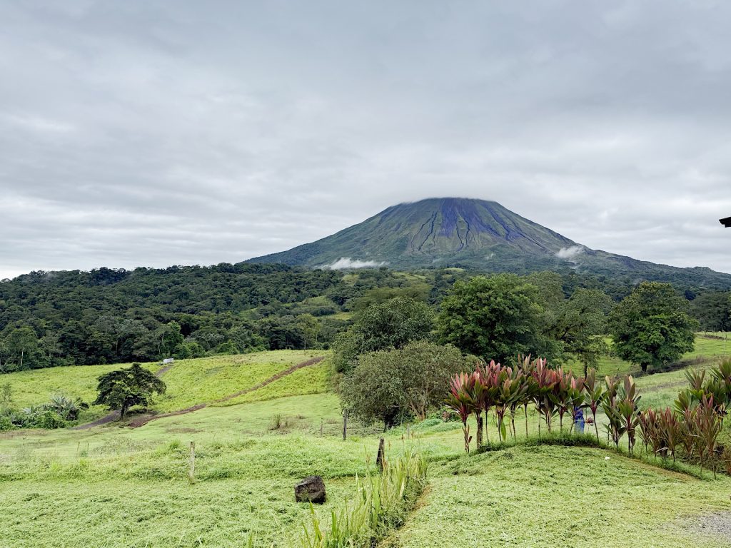 A lush green landscape with a prominent volcano in the background under a cloudy sky.