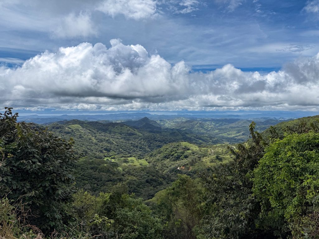 Scenic view of a lush green landscape with rolling hills under a partly cloudy sky.