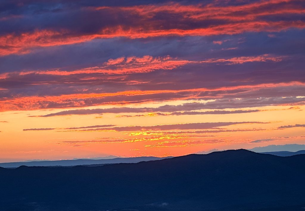 Vibrant sunset with orange and pink clouds over silhouette of distant mountains.