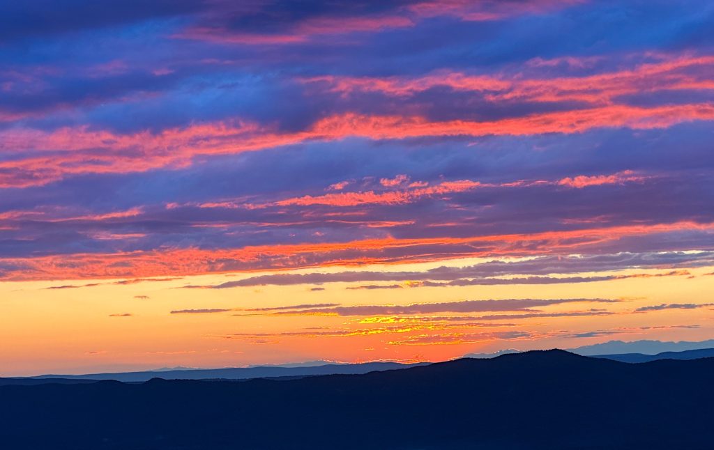 Vibrant sunset with purple and orange hues over silhouetted mountains and scattered clouds.